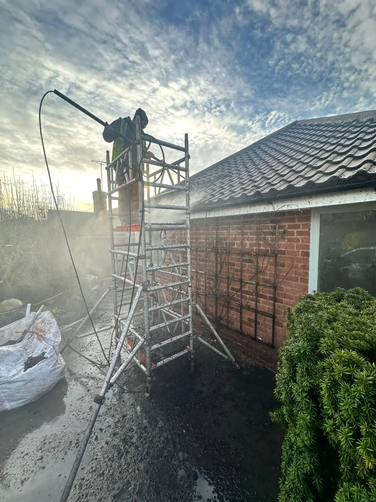 Operative on scaffolding pressure washing roof tiles during professional roof cleaning