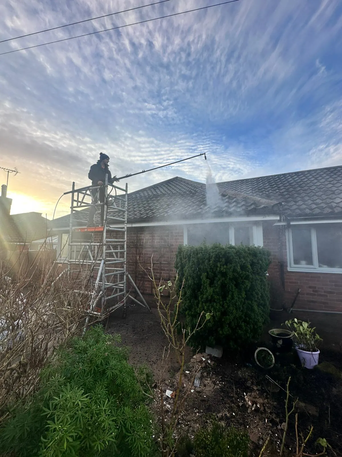 Roof cleaning in progress with operative using lance from scaffolding tower at sunset
