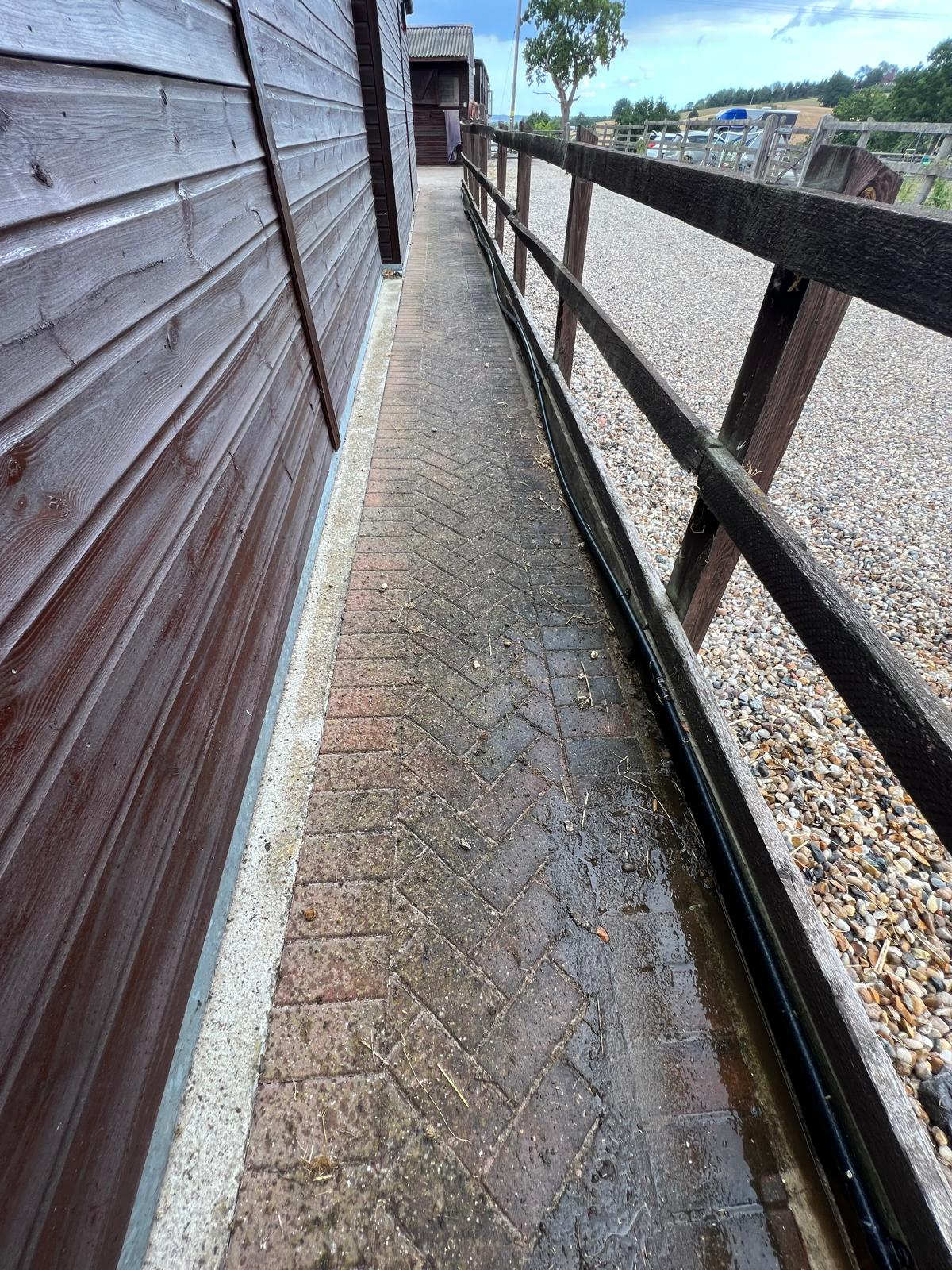 Dirty herringbone block paving stable path covered in dirt and algae before pressure washing