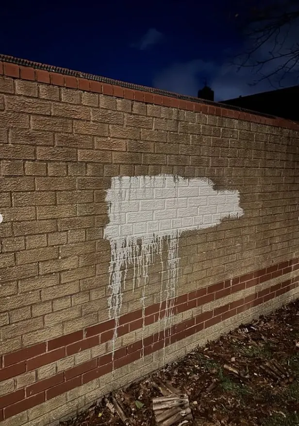 White masonry paint patch on brick boundary wall before paint removal