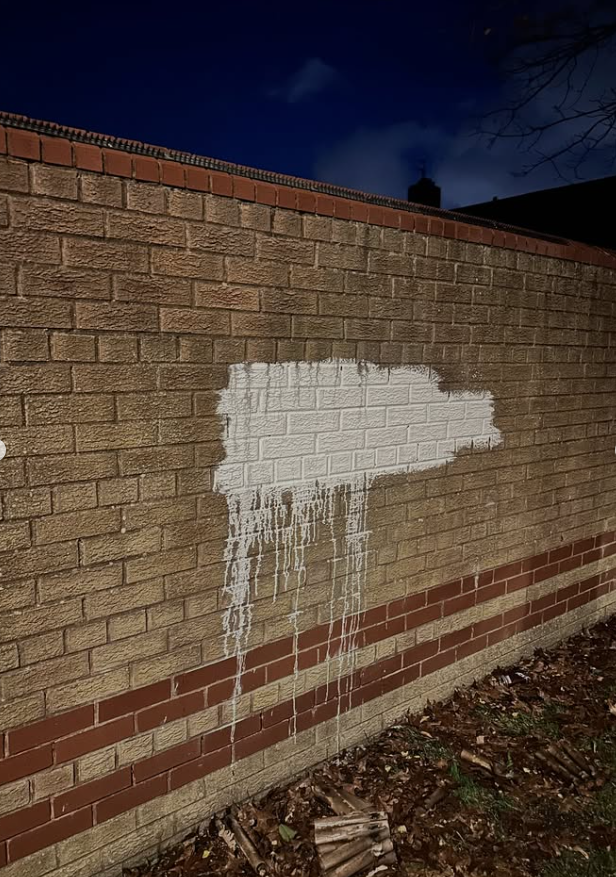 White masonry paint patch on brick boundary wall before paint removal