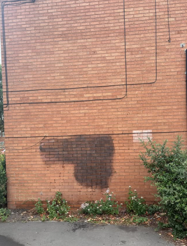 Large black spray paint graffiti tag on red brick wall requiring professional graffiti removal